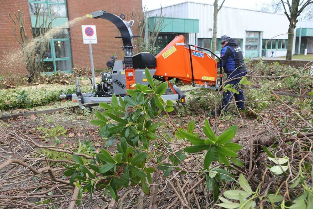 Ein Mann benutzt eine Maschine, um Äste in einem Garten zu zerkleinern.