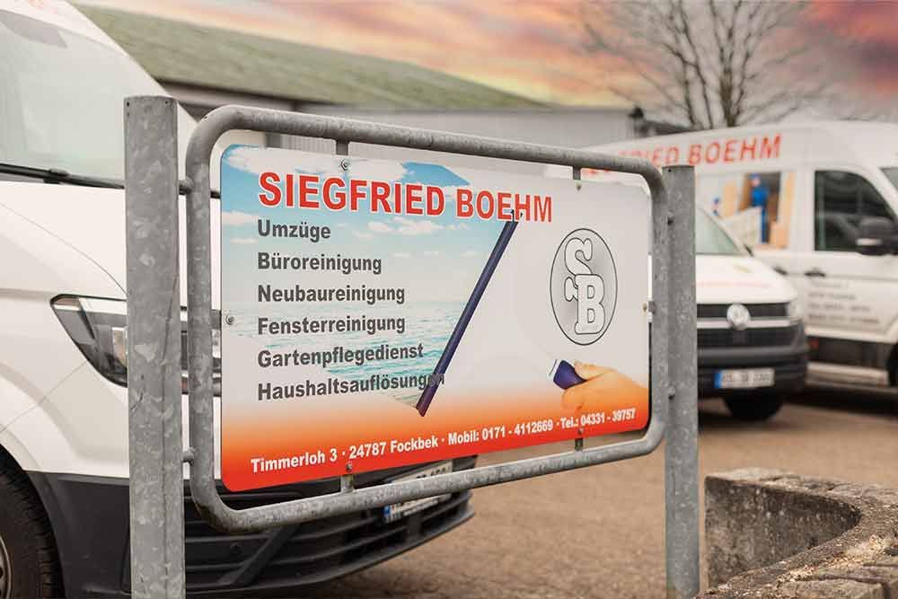 Ein weißer Lieferwagen parkt vor einem Schild mit der Aufschrift „Siegfried Böhm“.