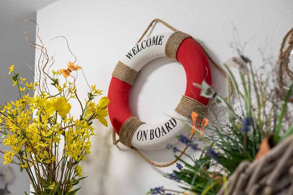 An einer Wand hängt neben Blumen ein Rettungsring.