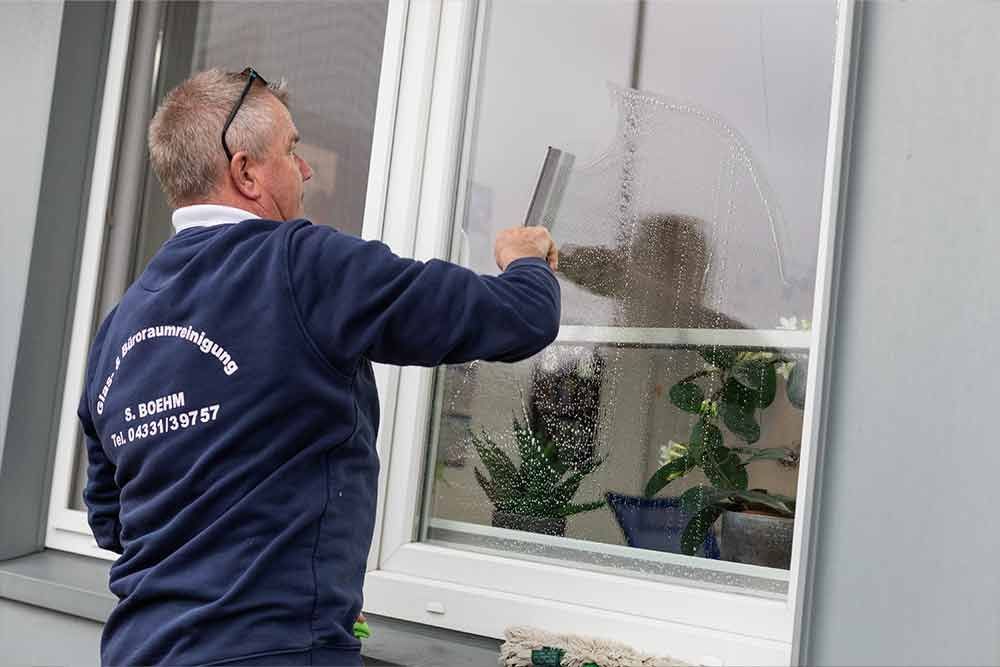 Ein Mann putzt ein Fenster mit einem Abzieher.