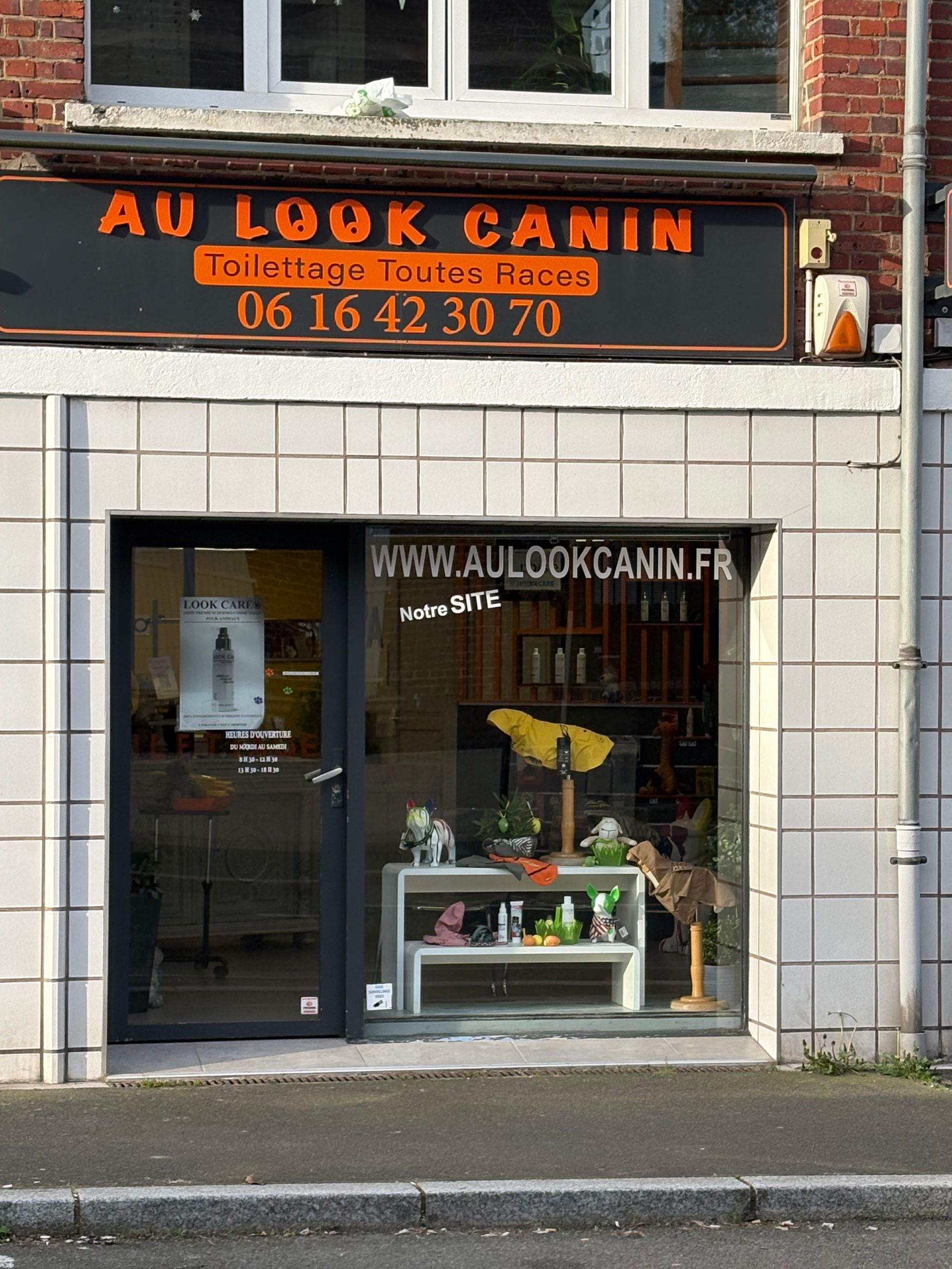 Façade du magasin Au Look Canin, un salon de toilettage pour animaux, avec une enseigne noire, un texte orange et une vitrine présentant les produits.