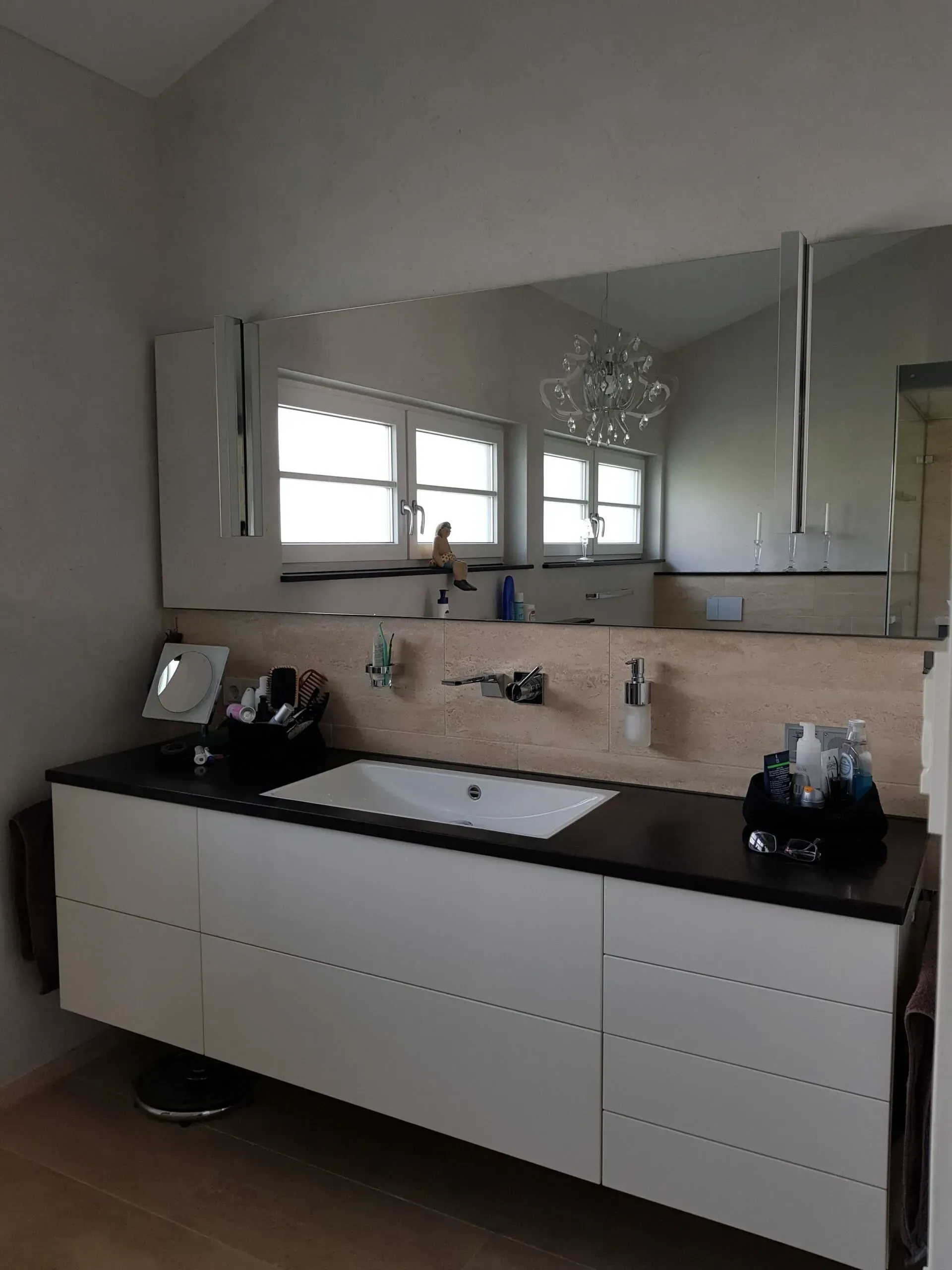 Badezimmermöbel mit großem Spiegel, weißen Schränken, schwarzer Arbeitsplatte und Fenster über dem Waschbecken