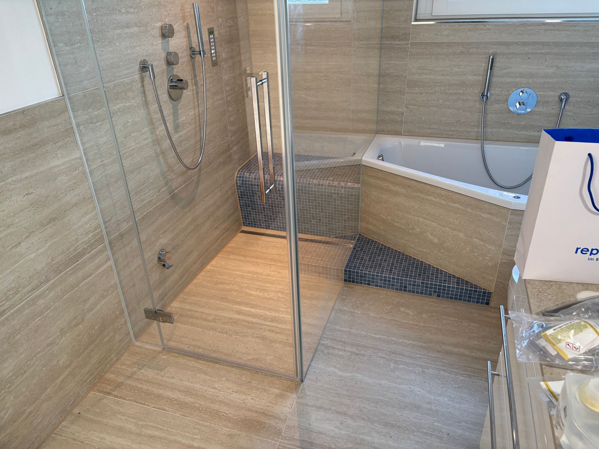 Modernes Badezimmer mit ebenerdiger Dusche, Glasabtrennung, beigefarbenen Fliesen und Badewanne auf der rechten Seite.