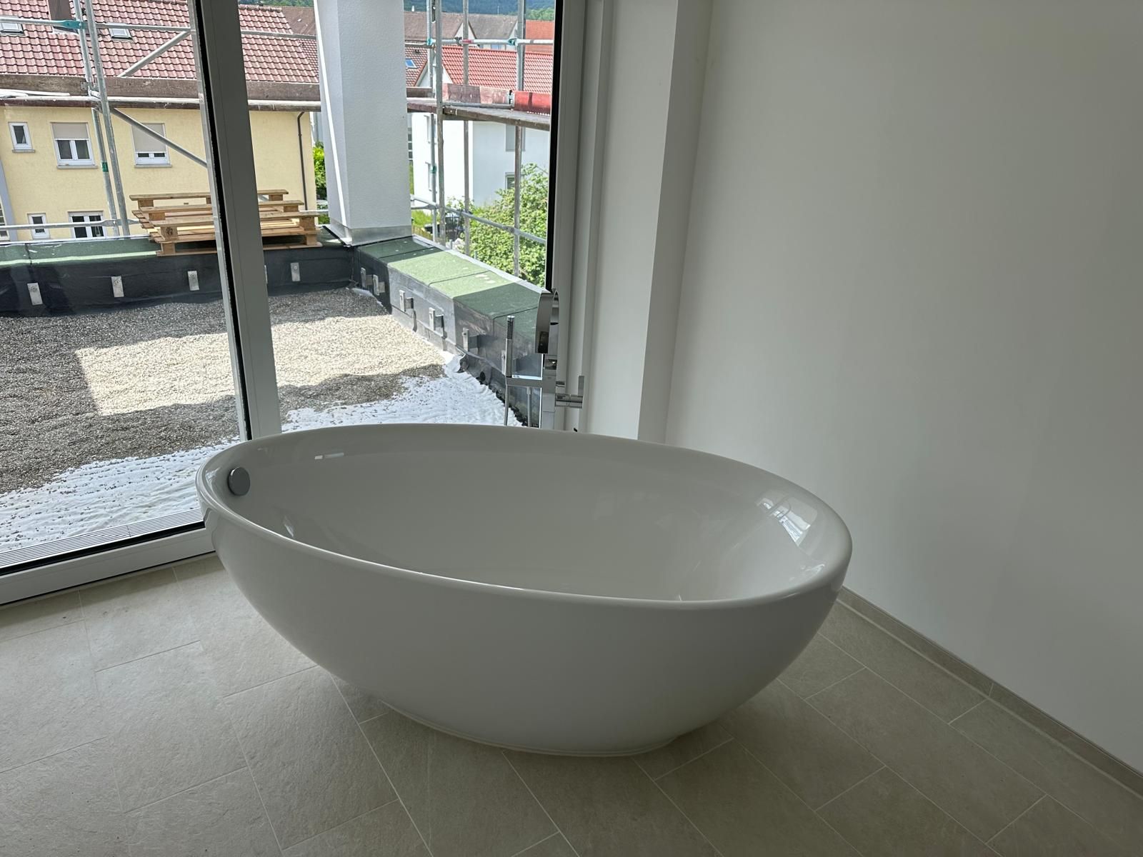 Moderne, freistehende weiße Badewanne neben einem großen Fenster in einem hellen Badezimmer