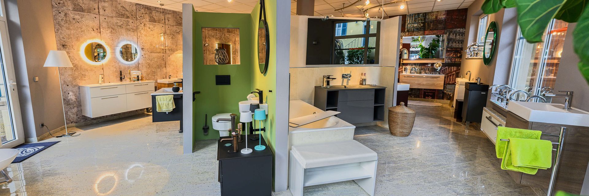 Badausstellung von Sanitär Paul, mit Badewanne, Waschtisch und Spiegelschrank, sowie eine grüne Wand und weitere Badmöbel