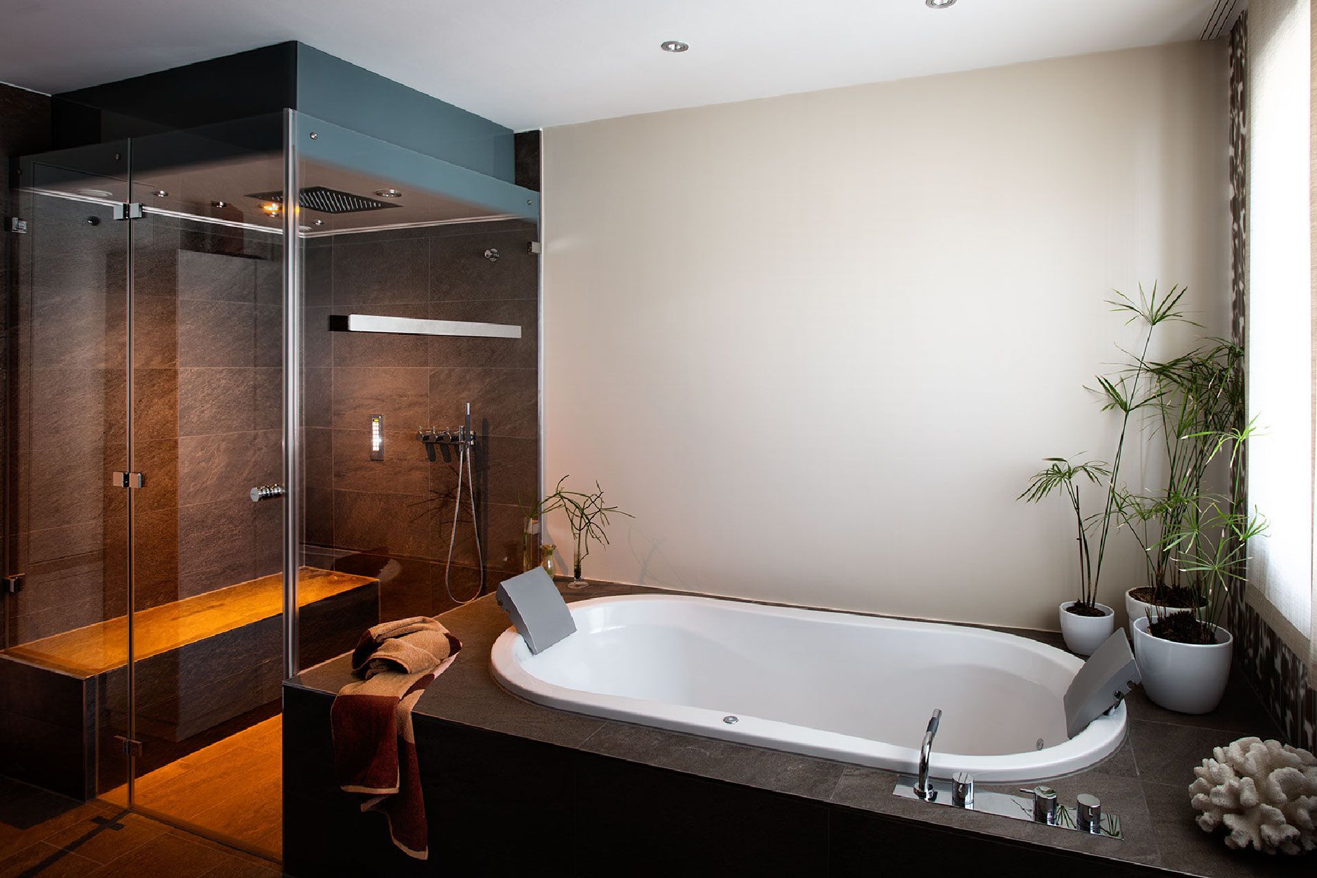 Modernes Badezimmer mit freistehender Badewanne, Glasdusche, warmer Beleuchtung und Topfpflanzen
