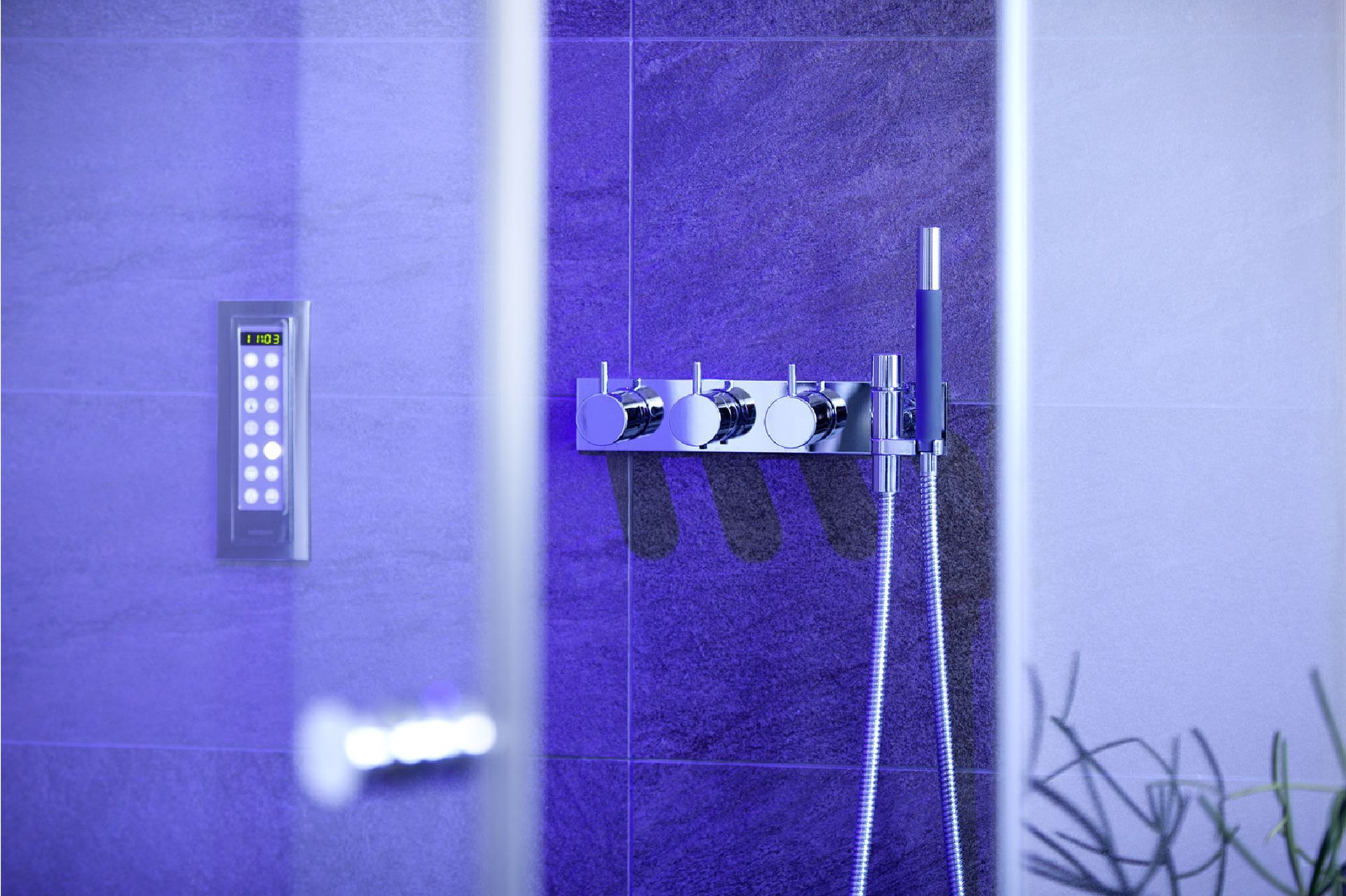 Blau beleuchtete Duschkabine mit Glastür, wandmontiertem Bedienfeld und Duscharmaturen.