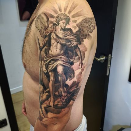 Un tatuaje detallado del Arcángel Miguel luchando contra el diablo en el brazo de un hombre.