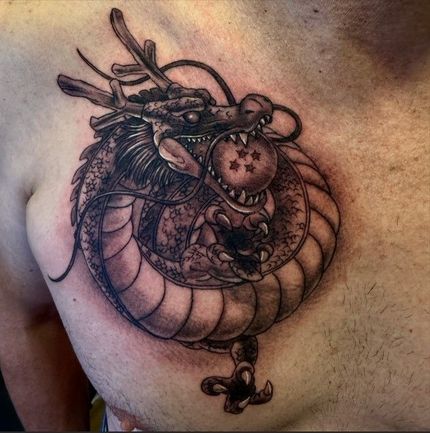 Tatuaje de dragón negro y gris en el pecho. El dragón sostiene una esfera estrellada en la boca.