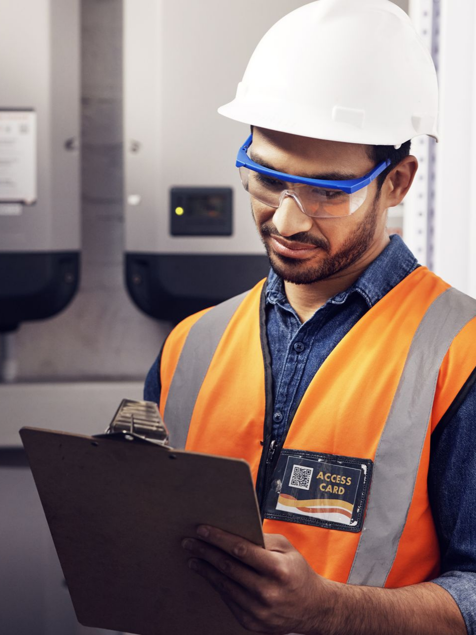 Un ouvrier portant un équipement de sécurité examine un bloc-notes près d'un équipement électrique.