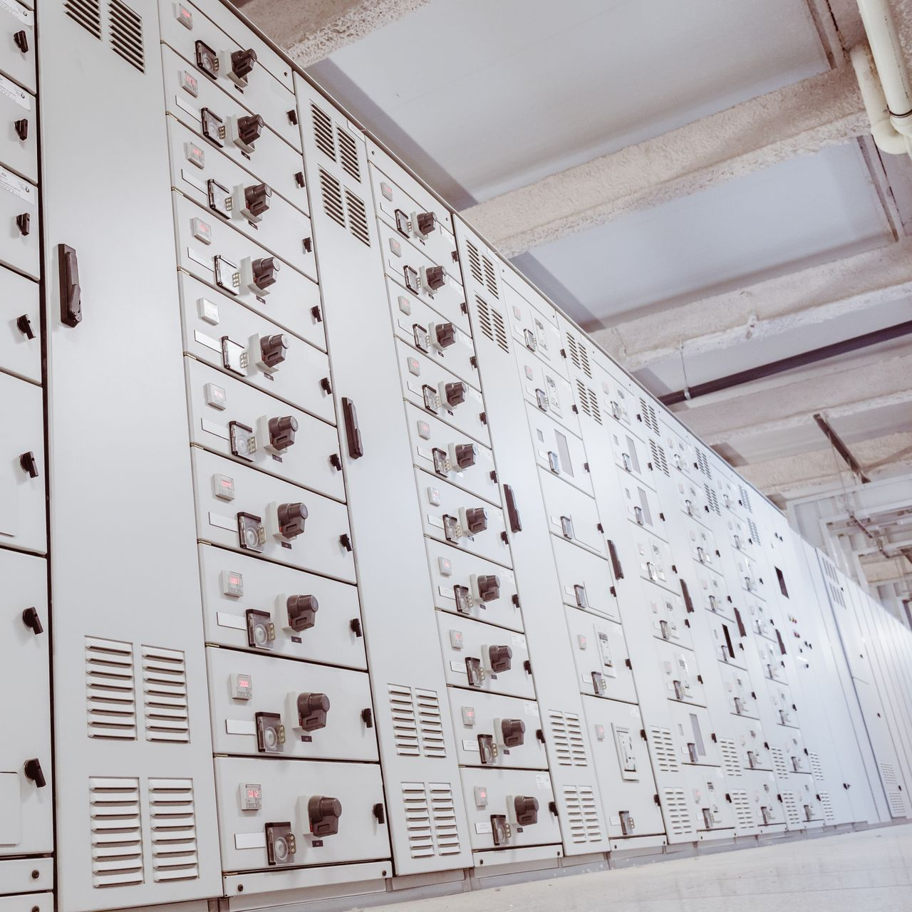 Rangée de tableaux électriques dans un local technique. Armoires métalliques grises avec divers interrupteurs et conduits d'aération.