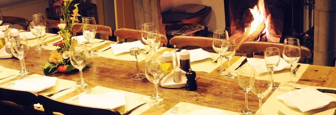 Un lungo tavolo con piatti, utensili e bicchieri da vino davanti al camino.