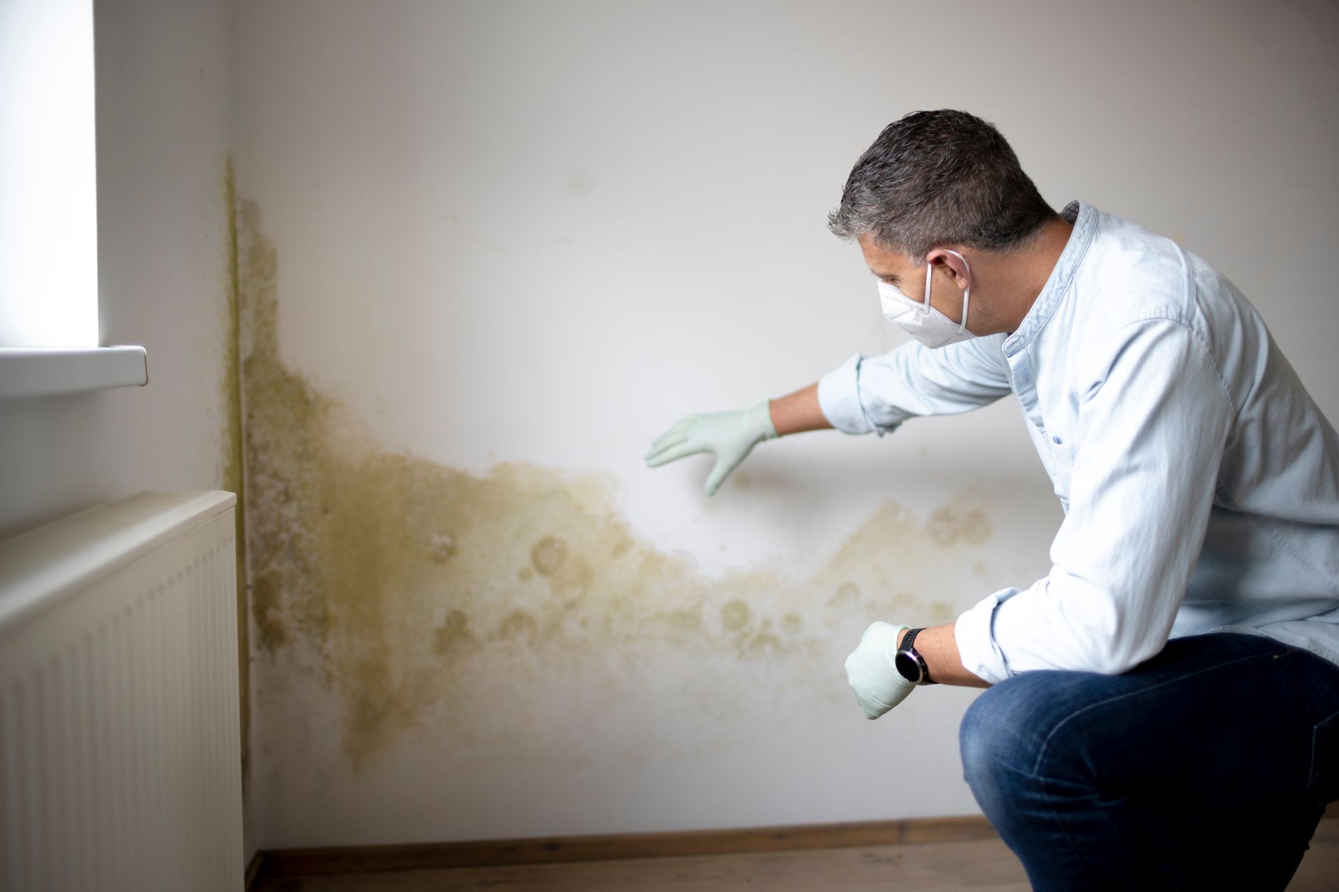 Homme avec un masque et des gants regardant un mur humide