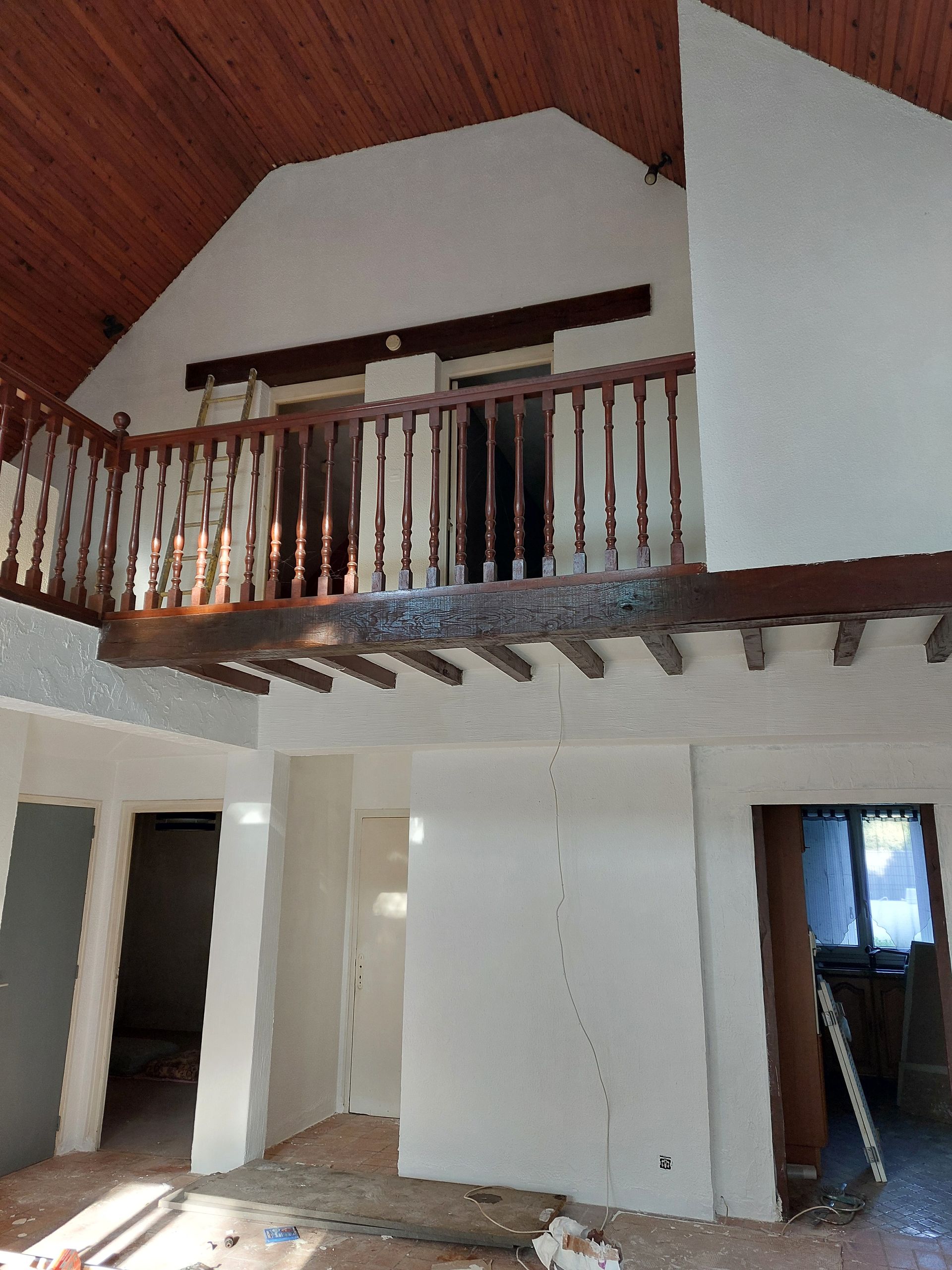 Vue intérieure d'une pièce rustique et inachevée, avec un balcon en bois, des poutres apparentes.