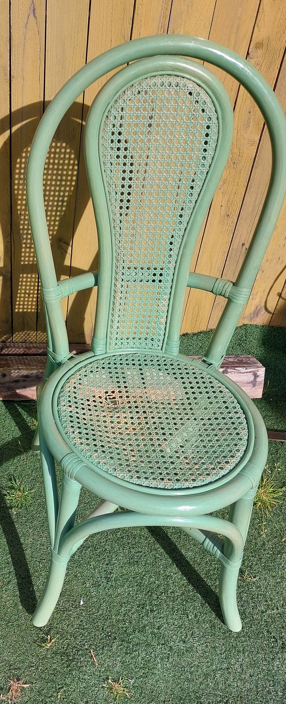 Une chaise en osier peinte en vert clair, avec un dossier et une assise arrondis abîmée.
