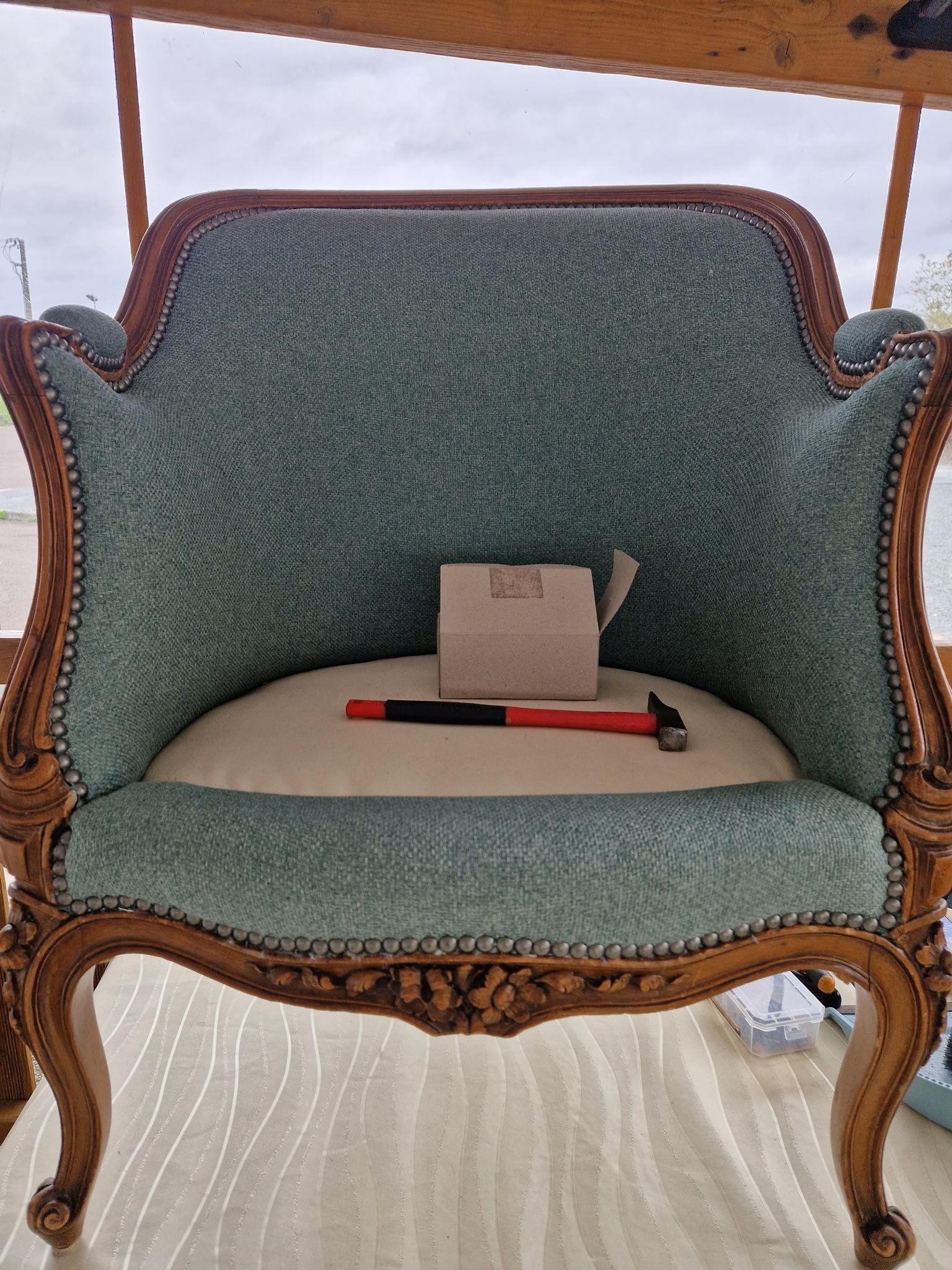 Un fauteuil orné, recouvert d'un tissu turquoise, avec des pieds en bois sculpté.