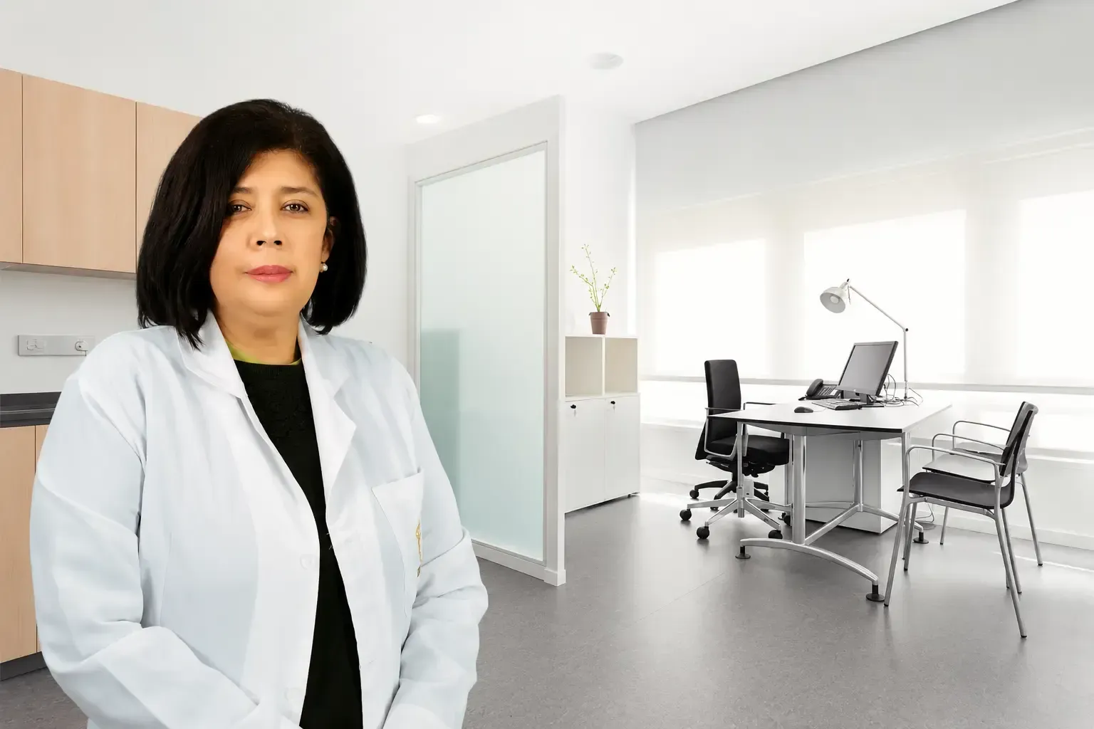 Mujer con bata blanca de pie en una oficina moderna con escritorio, sillas y ventanas luminosas.