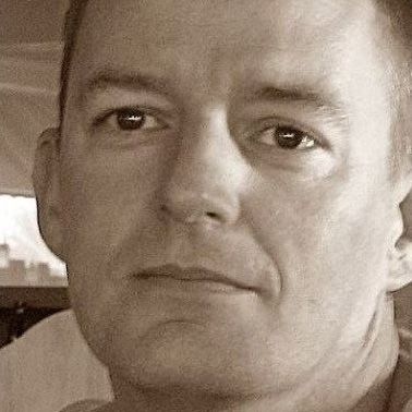 Nahaufnahme eines Sepia-Porträts eines Mannes mit kurzen Haaren, der direkt in die Kamera blickt.