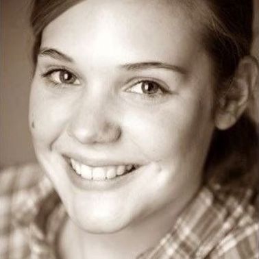 Lächelnde Frau, Nahaufnahme. Sie hat helle Haut, braune Augen und ein Grübchen auf der Wange. Sie trägt ein kariertes Hemd.