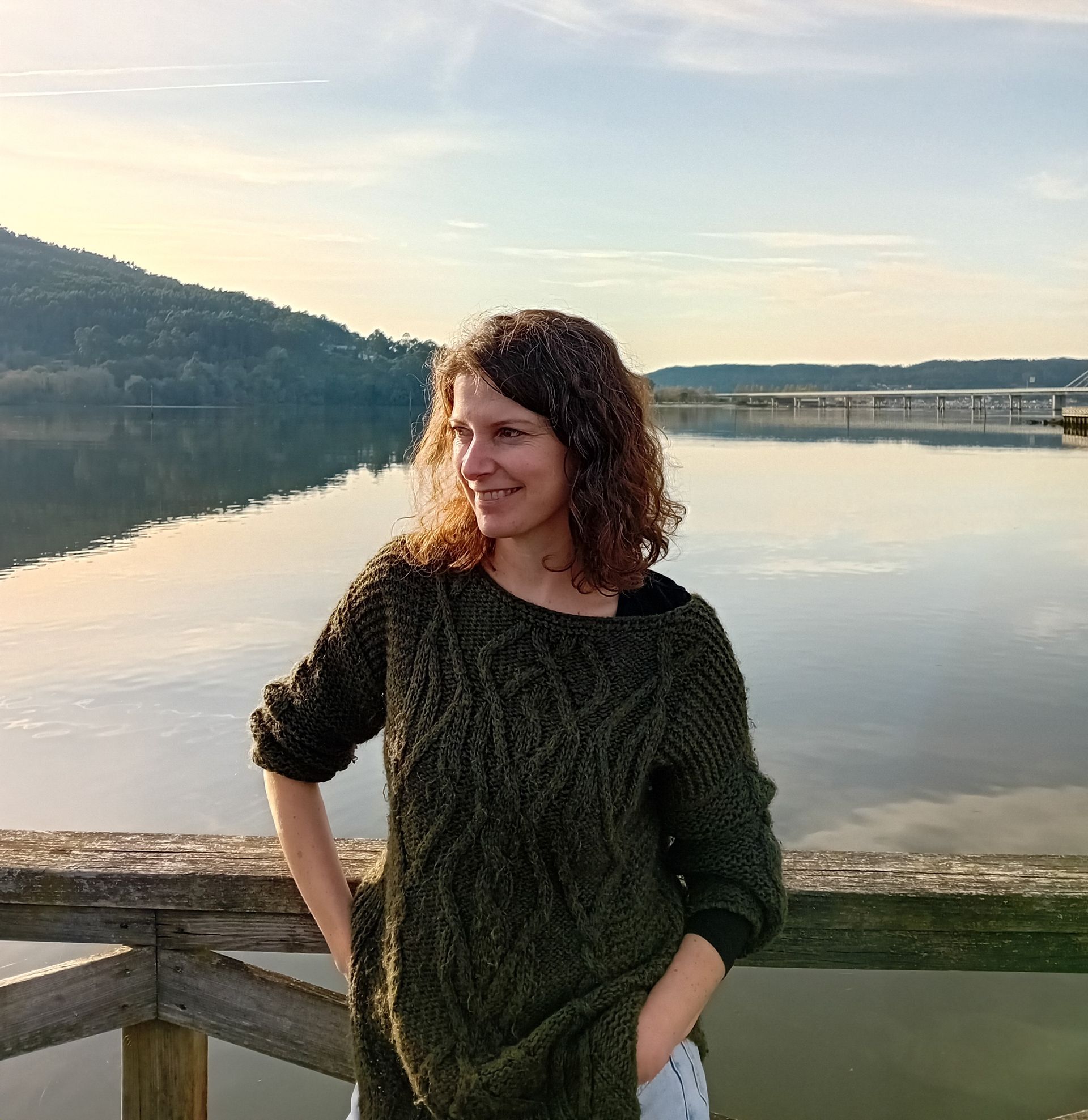 Una mujer con un suéter verde está parada junto a un cuerpo de agua.