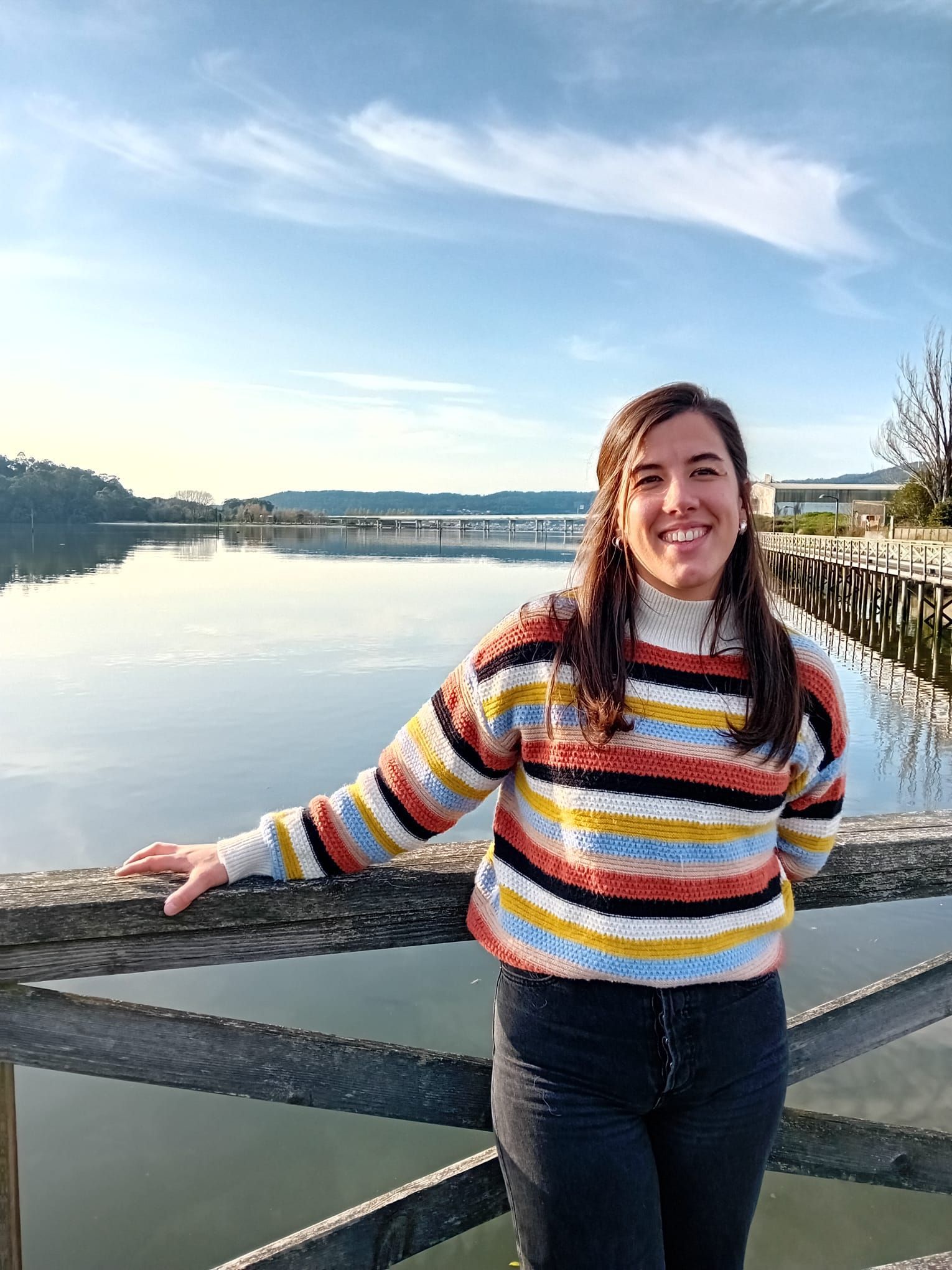 Una mujer con un suéter de rayas está parada en un puente con vistas a un lago.