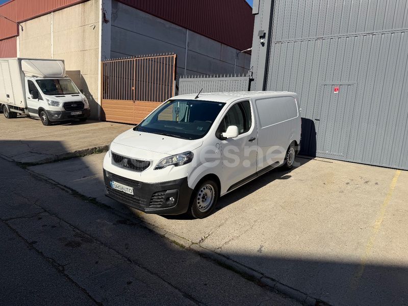 Furgoneta comercial blanca estacionada afuera de un edificio, otra furgoneta al fondo.