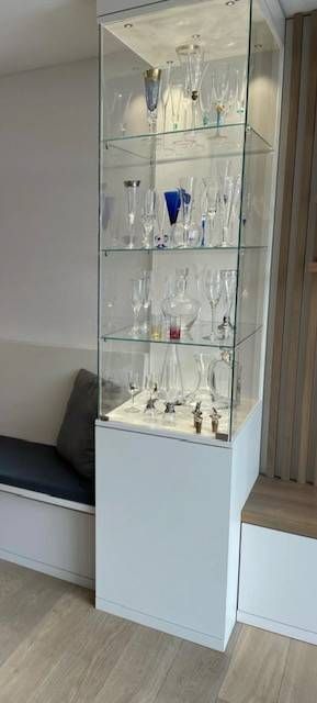 Eine Holz- und Glasvitrine voller Weingläser und -flaschen in einem Wohnzimmer. Foto von der Schreinerei Hanselmann GmbH