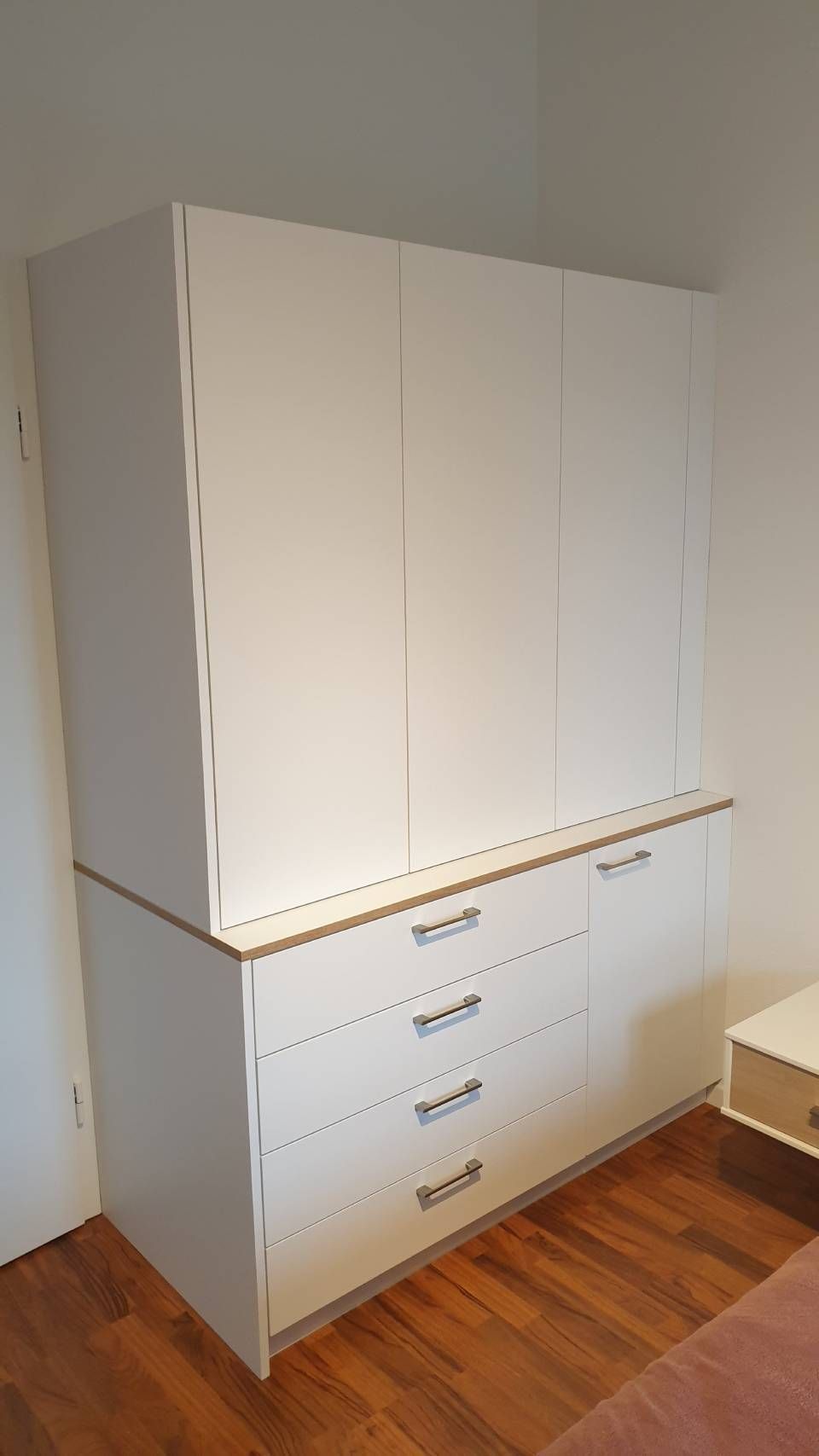 Ein weisser Kleiderschrank mit Schubladen und Türen in einem Schlafzimmer. Foto von der Schreinerei Hanselmann GmbH