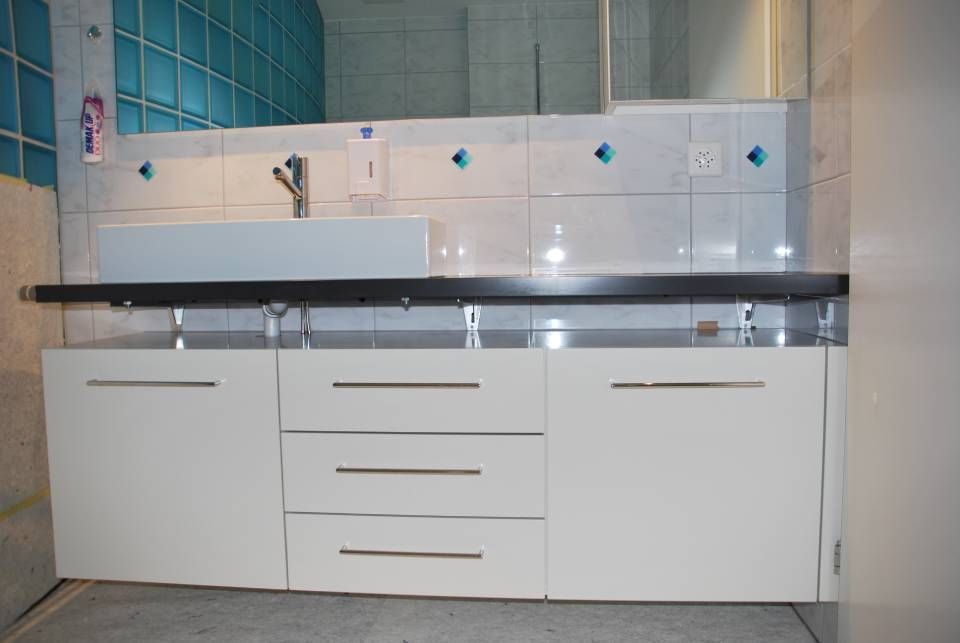 Ein Badezimmer mit weissen Schränken, einem Waschbecken und einem Spiegel. Foto von der Schreinerei Hanselmann GmbH