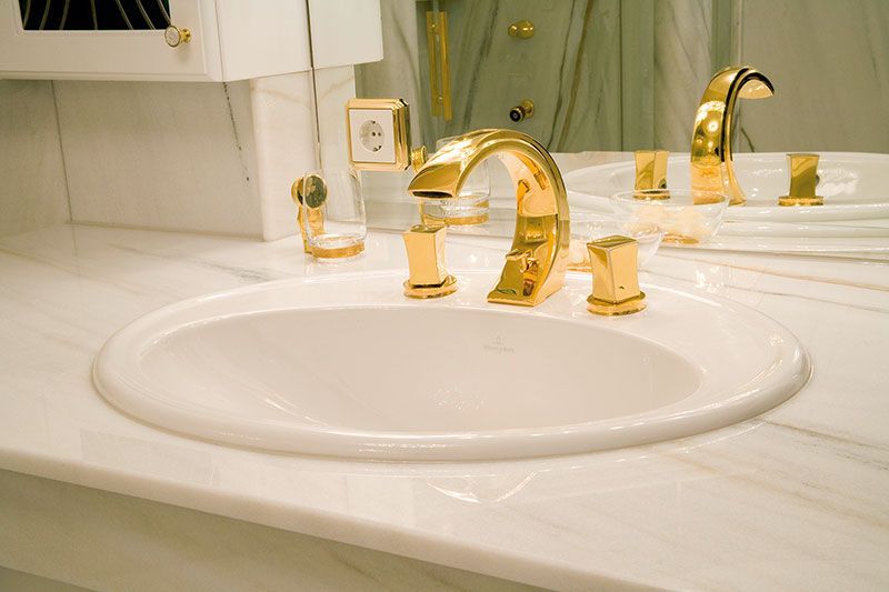 Ein Waschbecken mit goldenen Wasserhähnen und einem Spiegel.