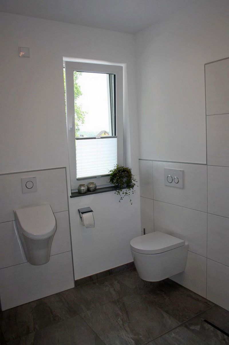 Ein Badezimmer mit Toilette, Urinal und Fenster.