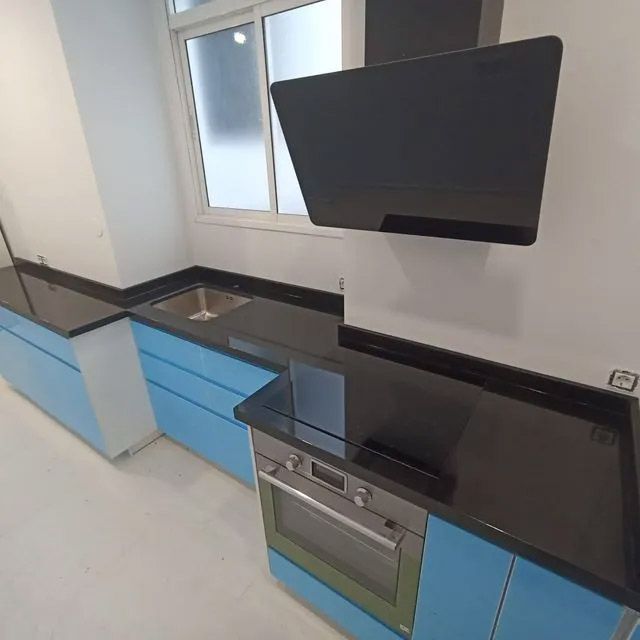 Cocina moderna con armarios azules, encimeras negras y un televisor montado en la pared encima de un horno.