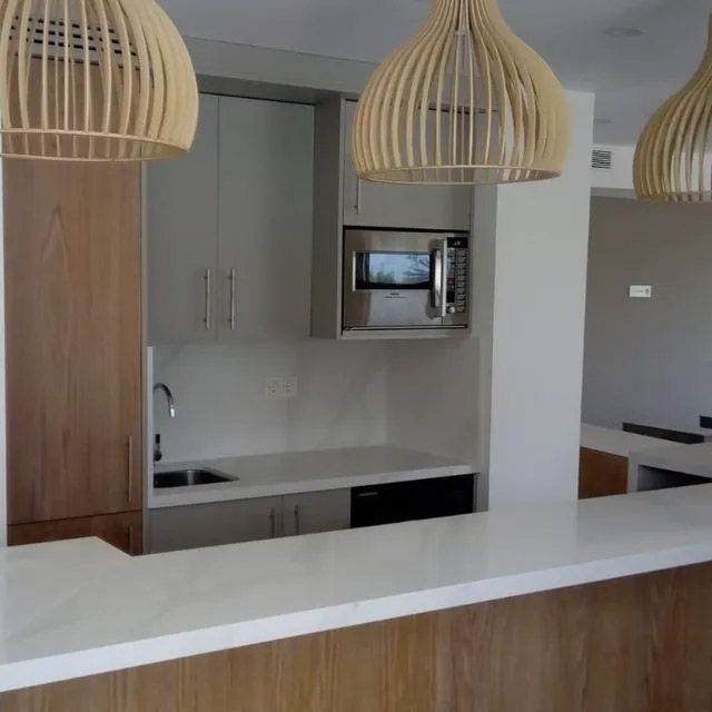 Cocina moderna con isla blanca, detalles de madera, lámparas colgantes y microondas integrado