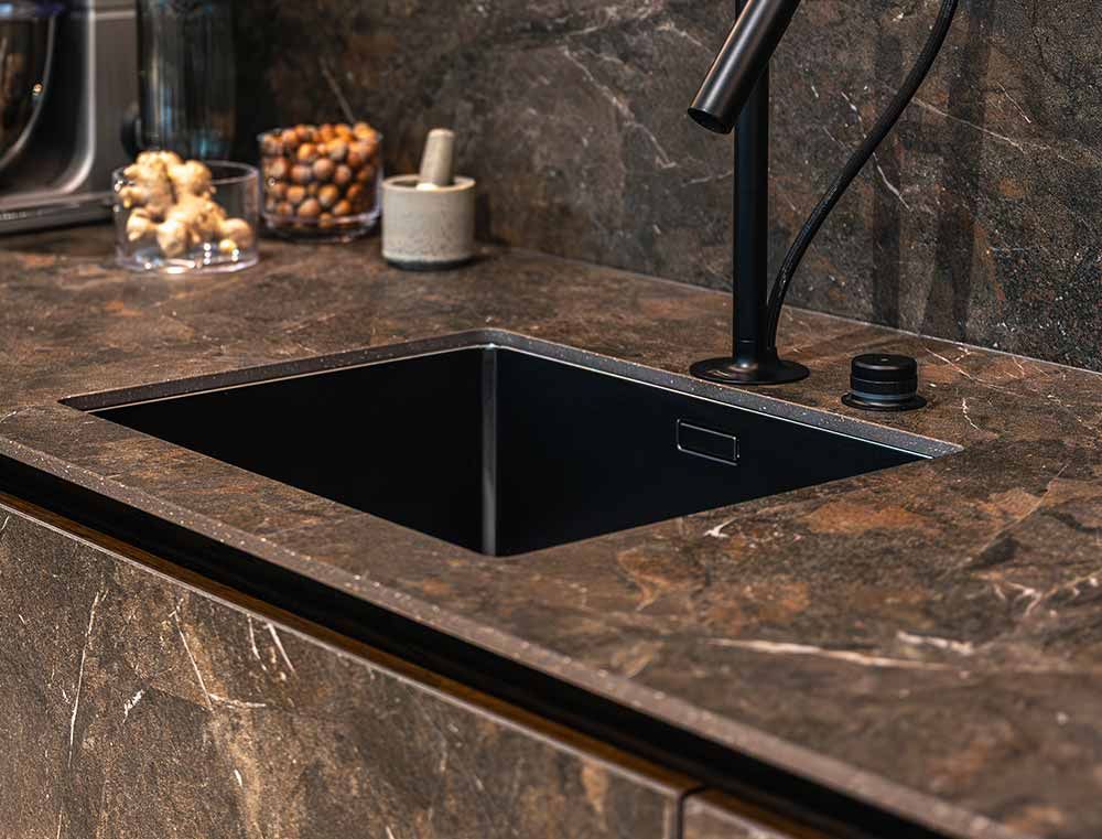 Encimera de cocina moderna con fregadero negro bajo encimera y grifo oscuro sobre superficies de piedra marrón