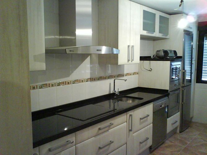 Una cocina con gabinetes blancos y encimeras negras.