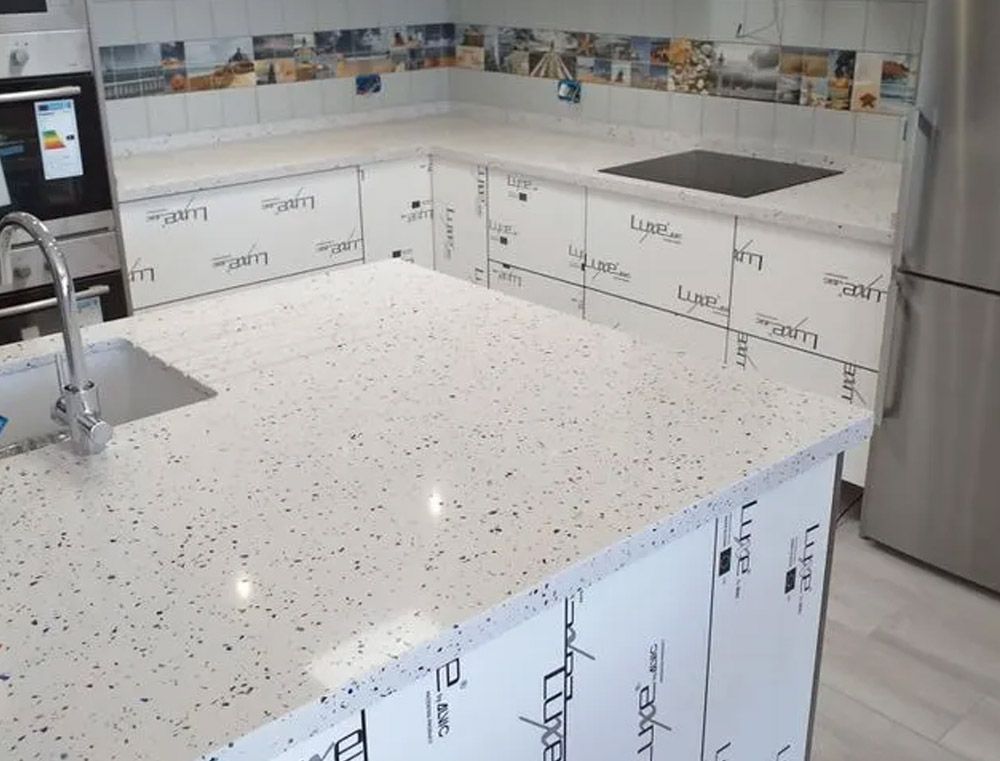 Cocina moderna con encimera de isla blanca moteada, fregadero, armarios y electrodomésticos de acero inoxidable