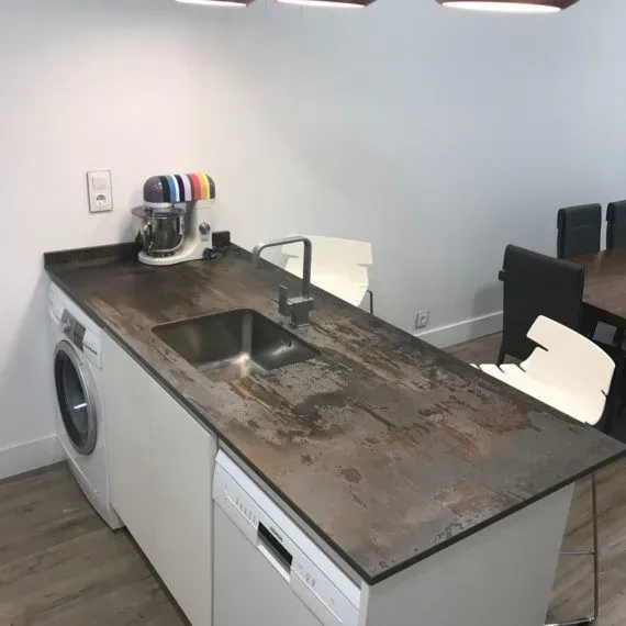 Cocina pequeña con una encimera desgastada, fregadero, lavadora y cafetera junto a una zona de comedor.