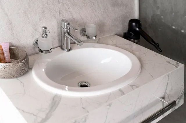 Lavabo de baño con encimera de mármol blanco y grifo, con dispensadores de jabón a un lado