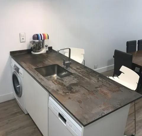 Cocina pequeña con la encimera dañada, un fregadero, un lavavajillas y una lavadora junto a la pared.