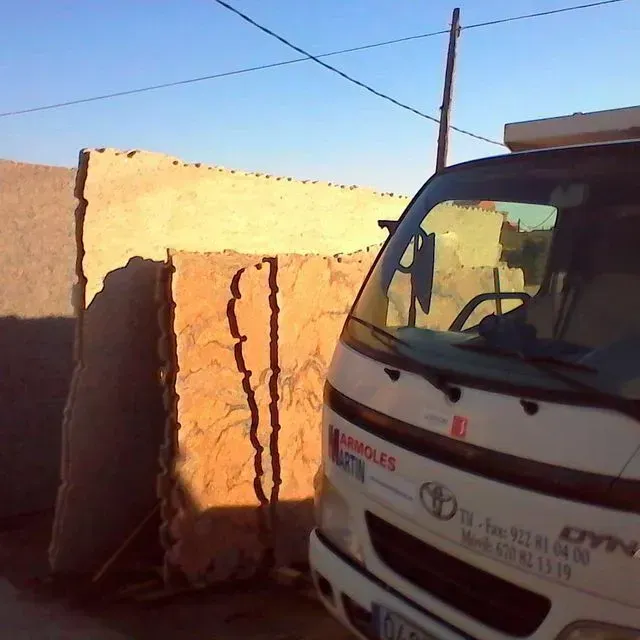 Camioneta Toyota blanca aparcada junto a una pared beige y una verja iluminadas por el sol, en una calle estrecha