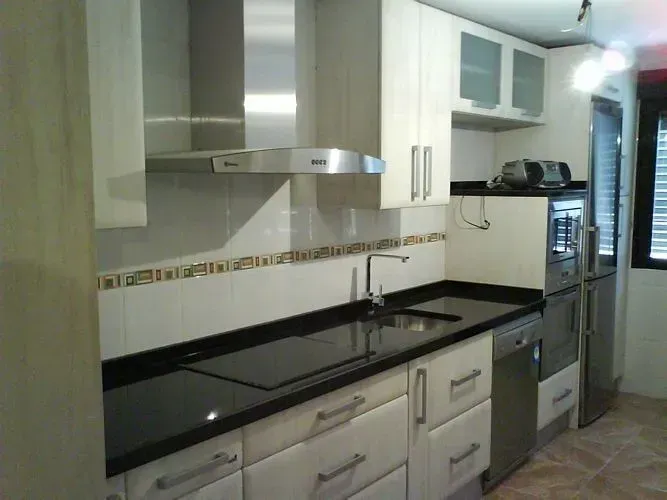 Cocina moderna con encimeras negras, armarios blancos y electrodomésticos de acero inoxidable