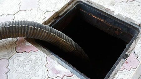Una tapa de alcantarilla de la que sale una manguera.