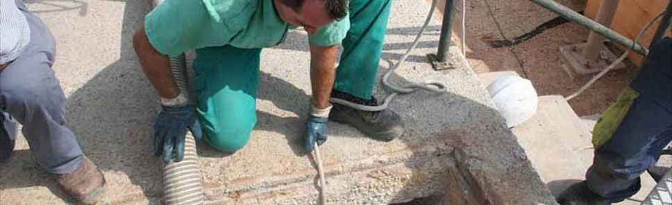 Un hombre está arrodillado junto a la tapa de una alcantarilla.