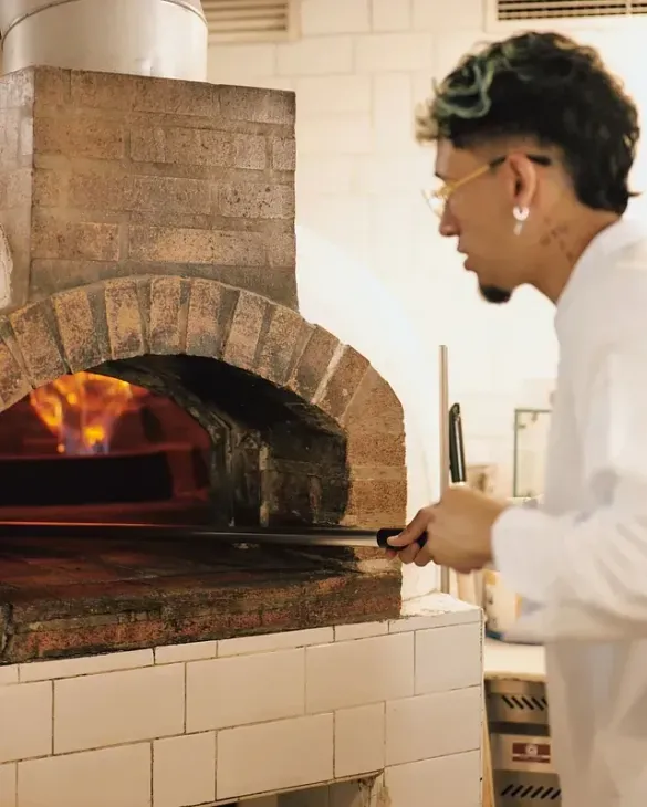 Un hombre está cocinando pizza en un horno de ladrillo.