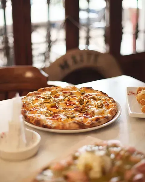Una pizza reposa en un plato blanco sobre una mesa.