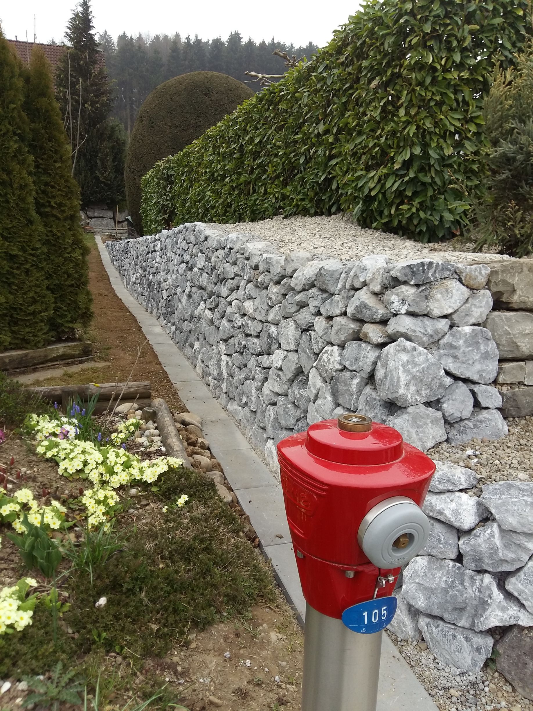 Neben einer Steinmauer steht ein roter Hydrant.