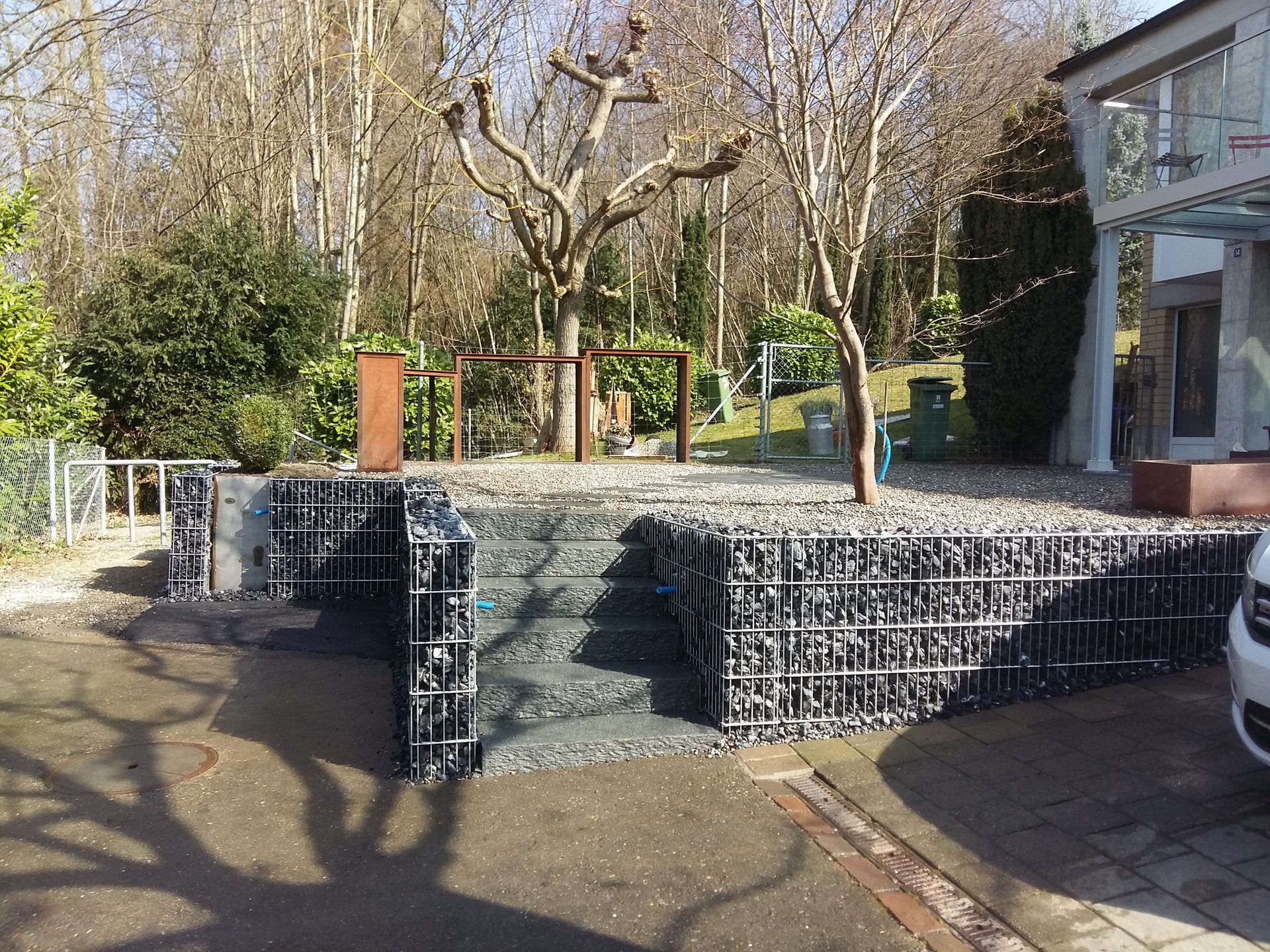 Vor einem Gebäude, zu dem eine Treppe hinaufführt, ist ein Auto geparkt.