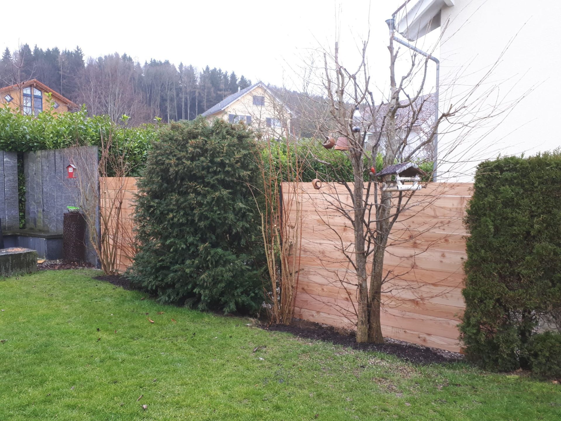 A wooden fence surrounds a lush green lawn in a backyard.