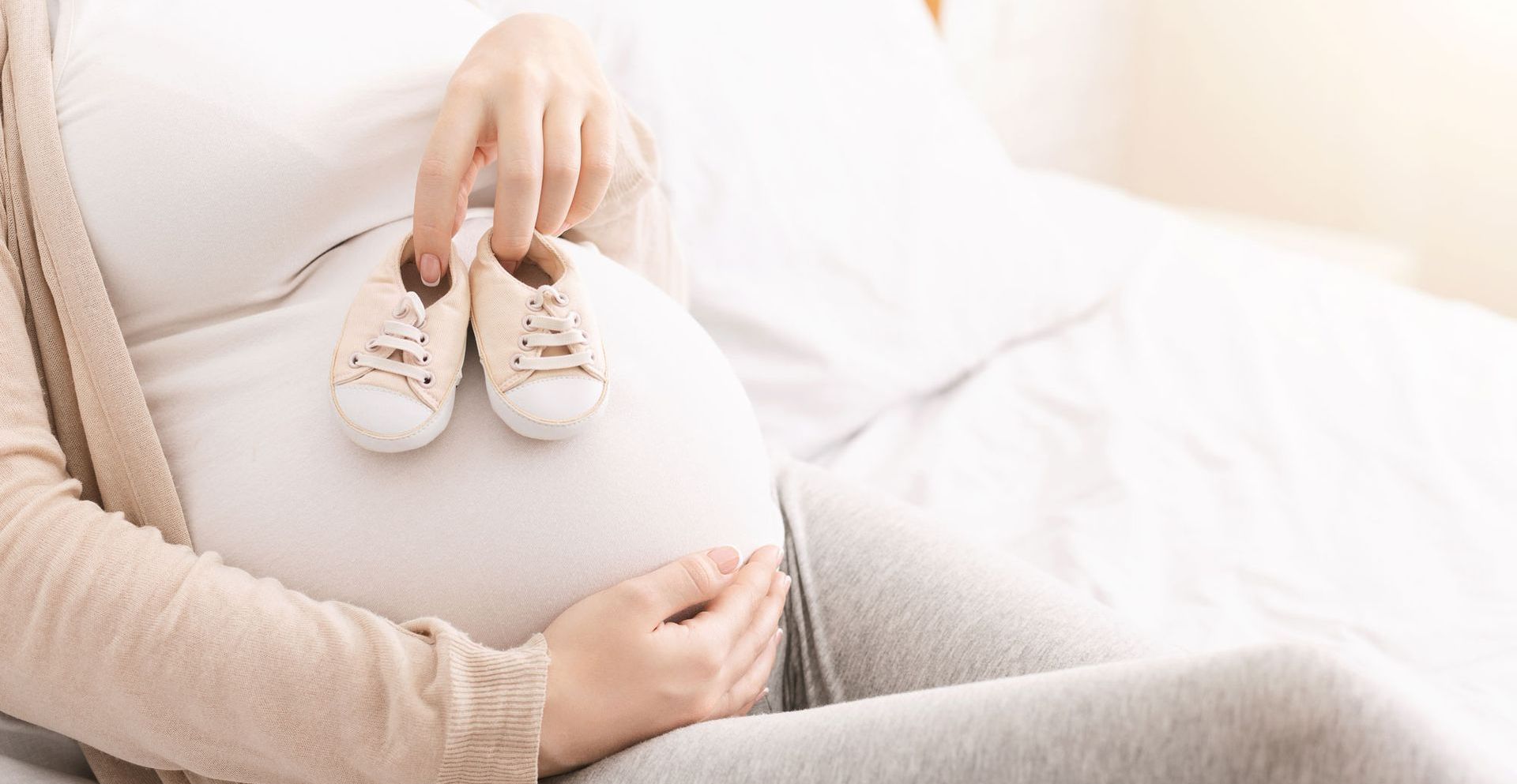 Une femme enceinte est assise sur un canapé tenant des vêtements de bébé et un animal en peluche.