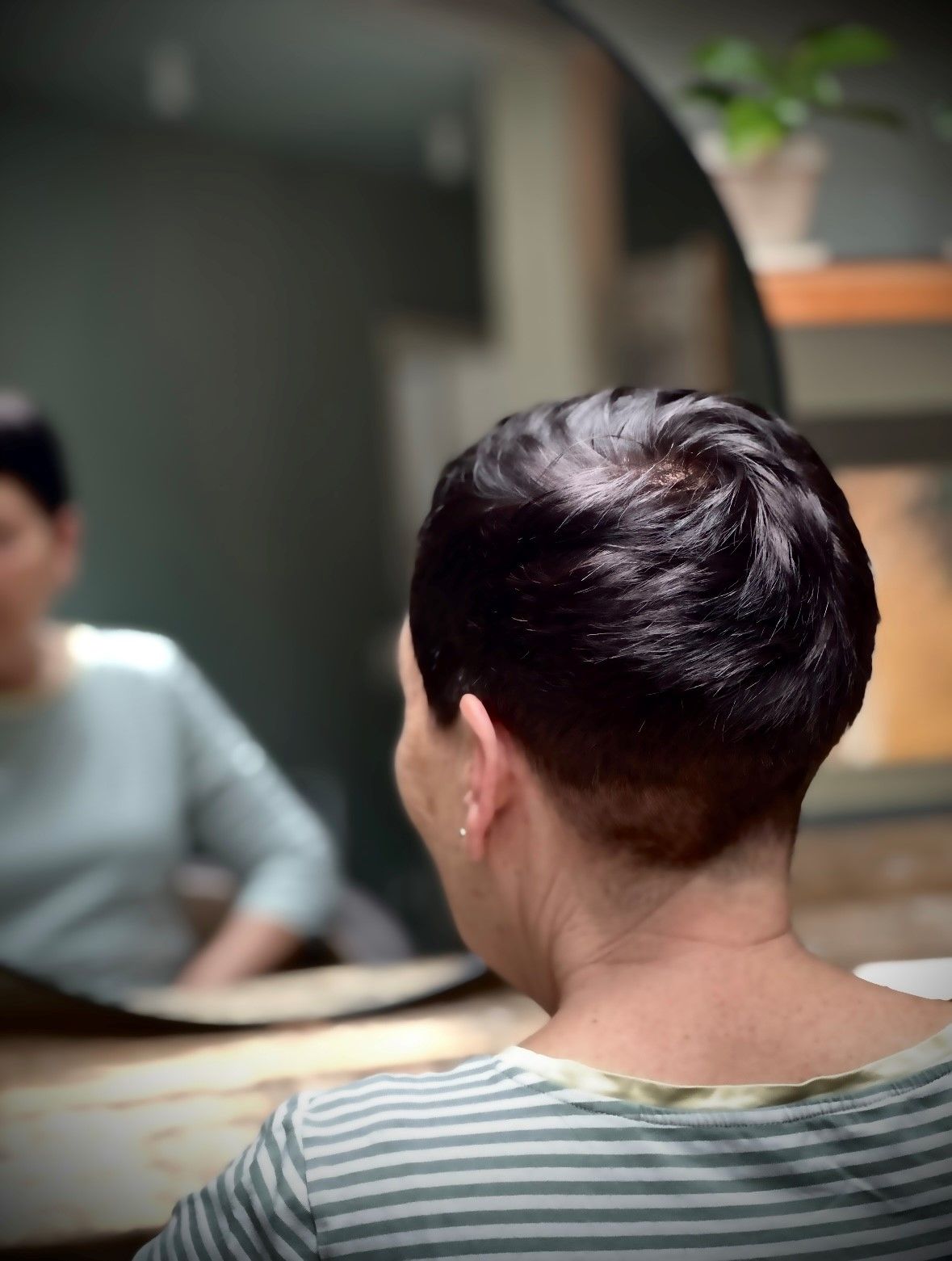 Eine Frau mit kurzen Haaren sitzt vor einem Spiegel.